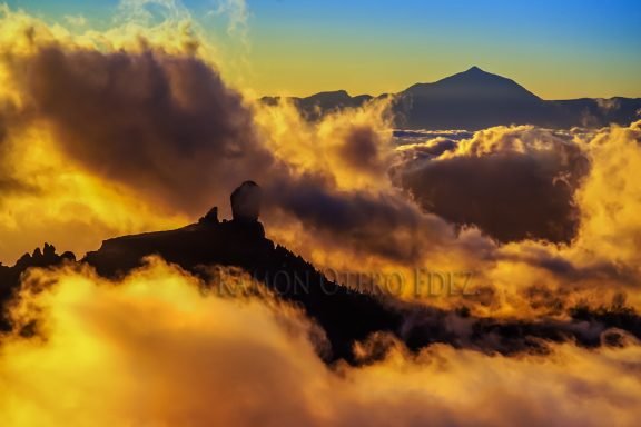 Vista de montañas y nubes anaranjadas al amanecer, con un pico visible al fondo.